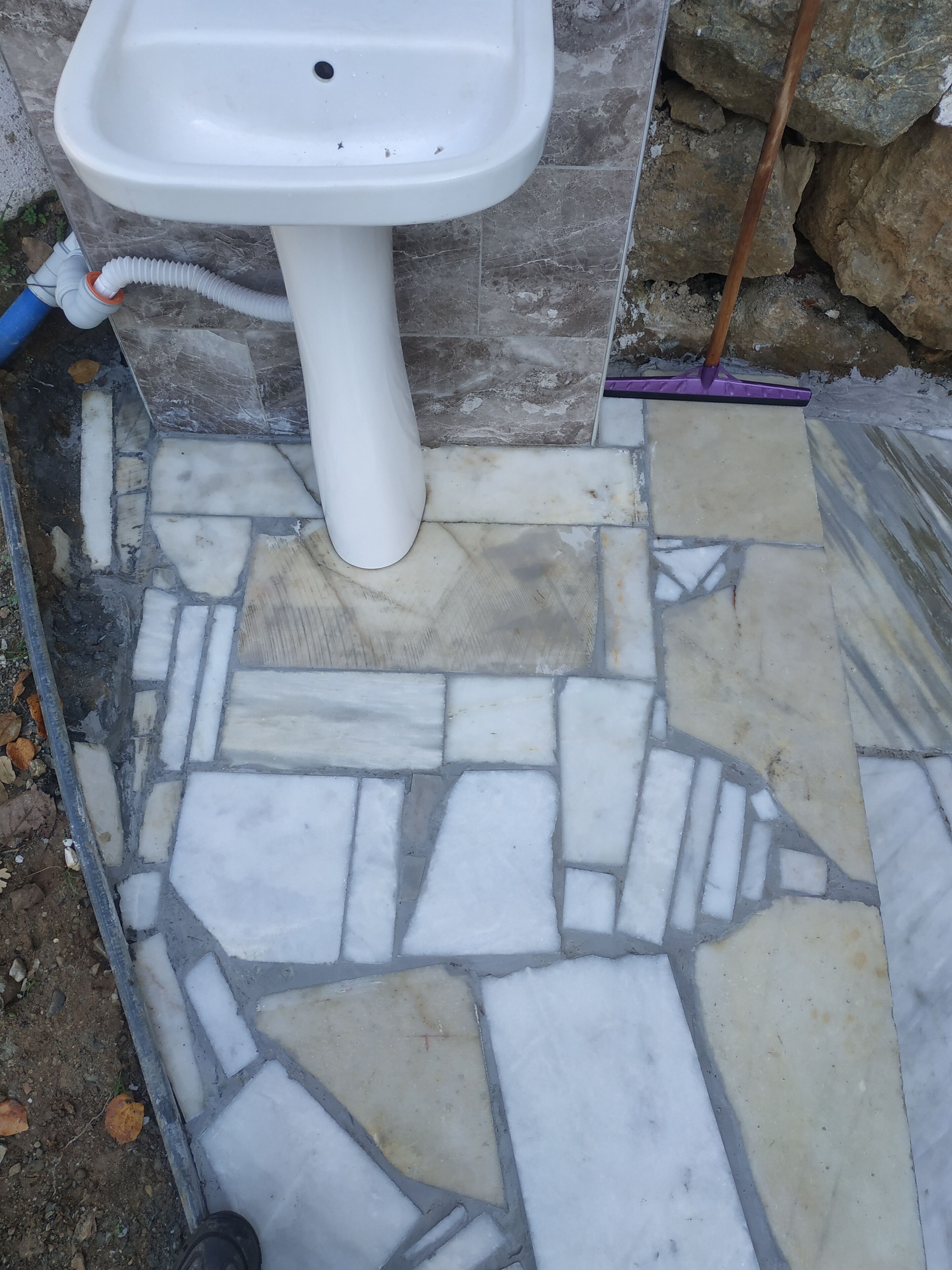 A bathroom with a white pedestal sink, tiled floor, and a stone wall.