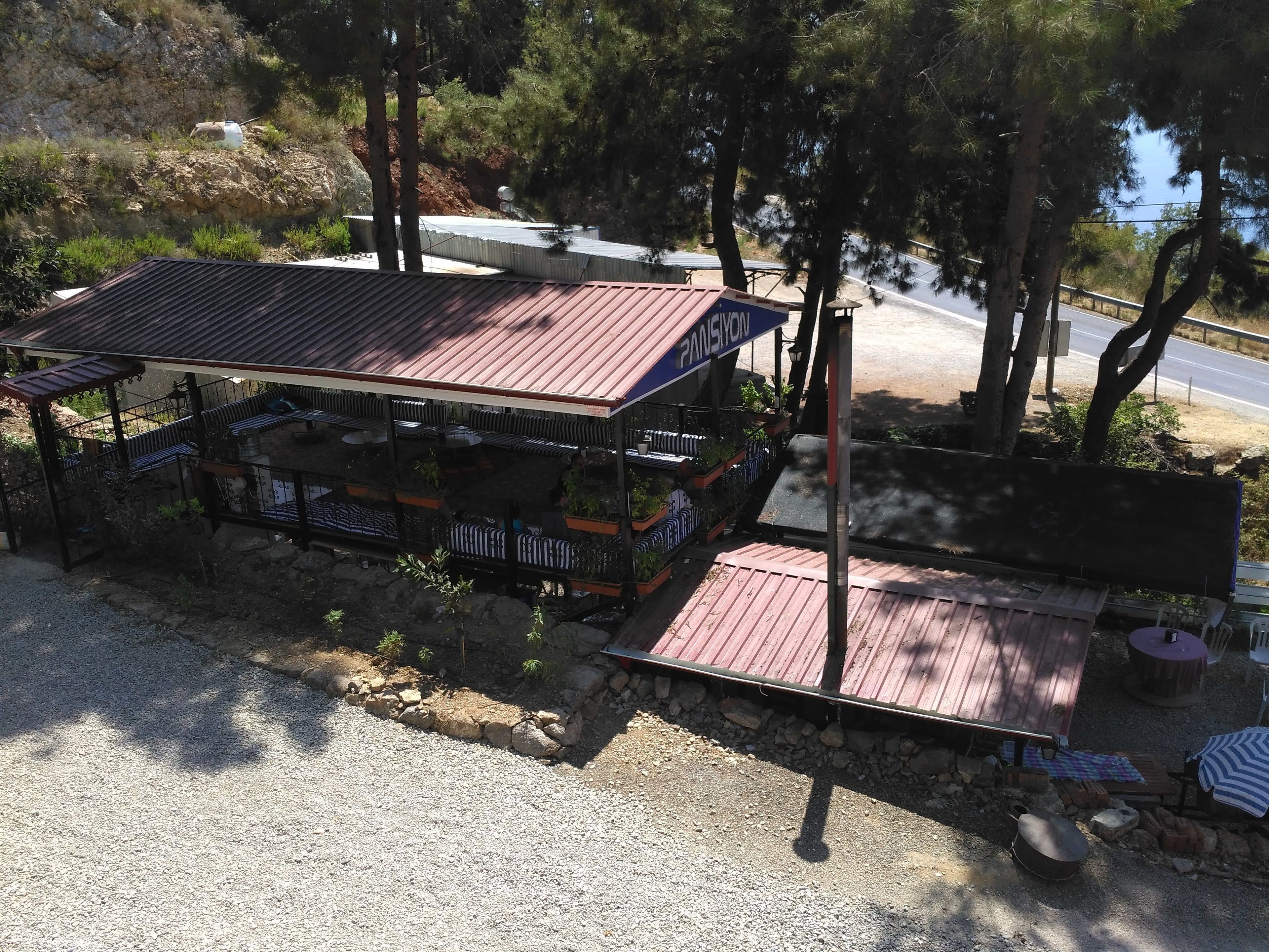 A two-story building with a metal roof, outdoor seating area, and a view of a road and trees.