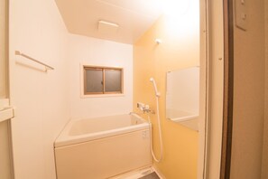 Une petite salle de bain avec une baignoire, une douche et une fenêtre.
