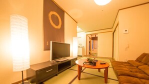 A hotel room with a TV, a small table with a plant, a sofa, and tatami mats. - Kyo Machiya Nijo (Kyoto)