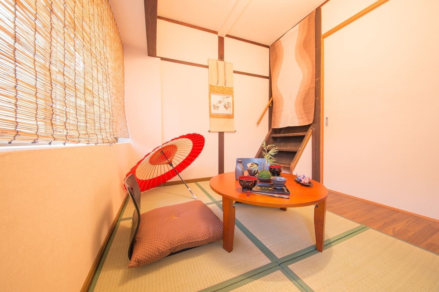 Habitació japonesa tradicional amb sòl de tatami, una taula baixa amb safata d'objectes, un ventall vermell i blanc, i una porta corredissa.