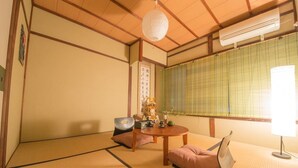 A traditional Japanese room with tatami flooring, a shoji screen, a tatami mat table, a low table with a cushion, and a hanging paper lantern. - Kyo Machiya Nijo (Kyoto)