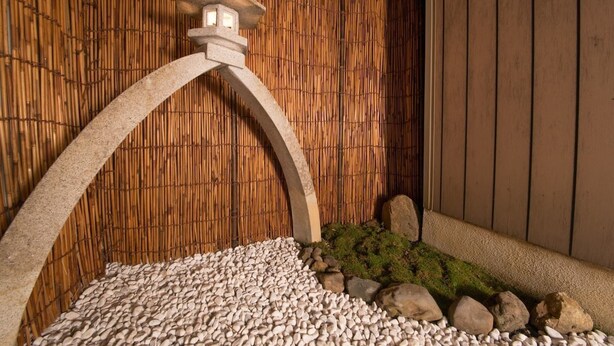 A stone lantern with a curved arch, a bamboo wall, and a pebbled ground with moss and rocks. - Kyo Machiya Nijo (Kyoto)