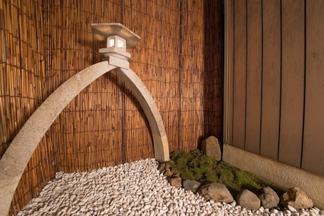 A stone lantern with a curved arch, a bamboo wall, and a pebbled ground with moss and rocks.