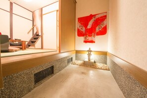 Une pièce de style japonais traditionnel, avec un sol recouvert de tatamis, une porte coulissante en papier de riz (shoji), une petite lanterne en pierre et un tissu rouge suspendu.