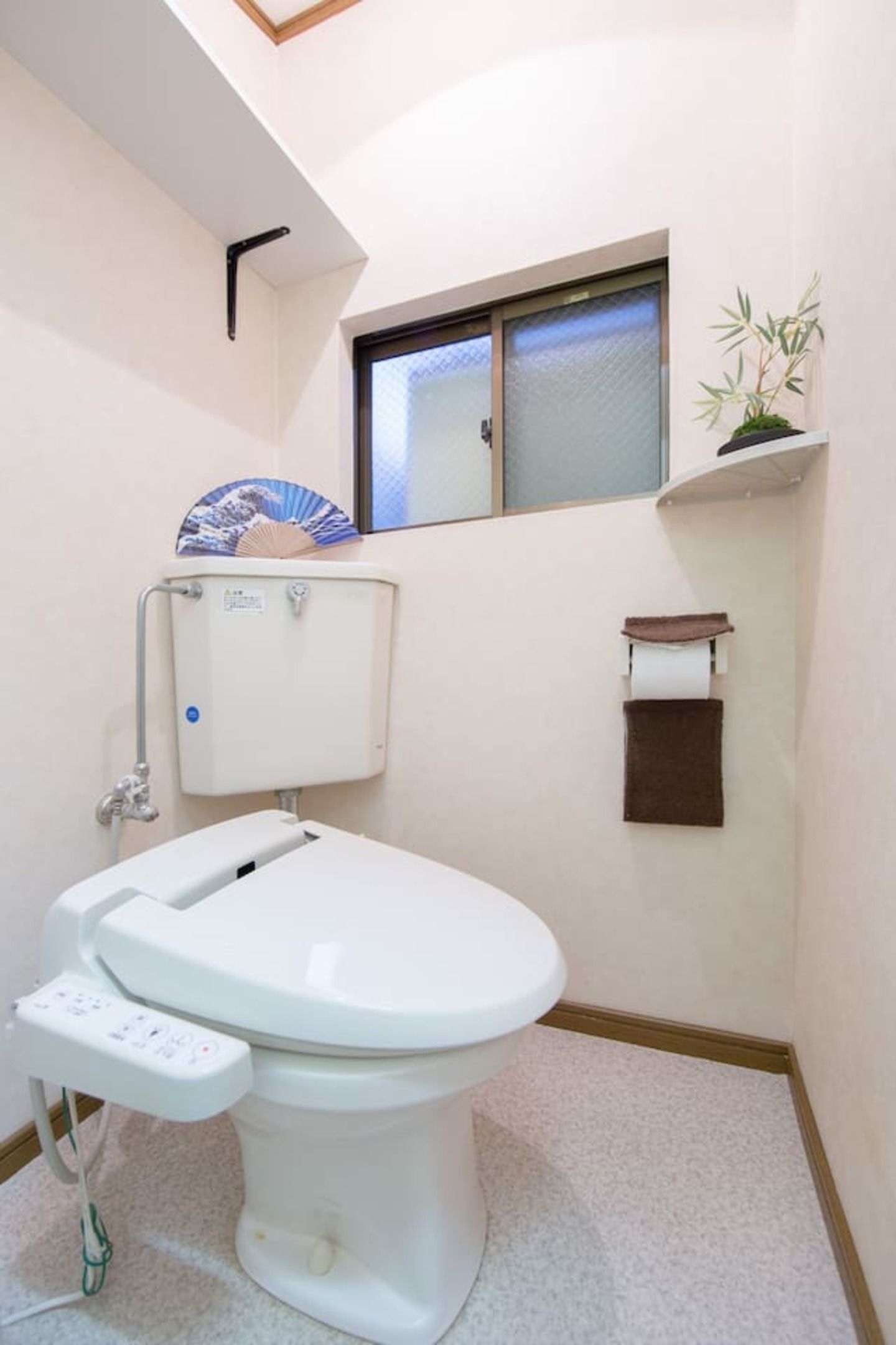 A small bathroom with a toilet, a window, and a shelf with a plant.