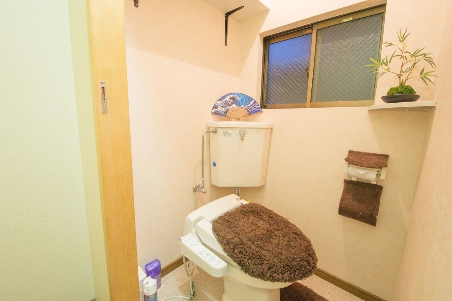 A small bathroom with a toilet, a window, and a shelf with a plant.