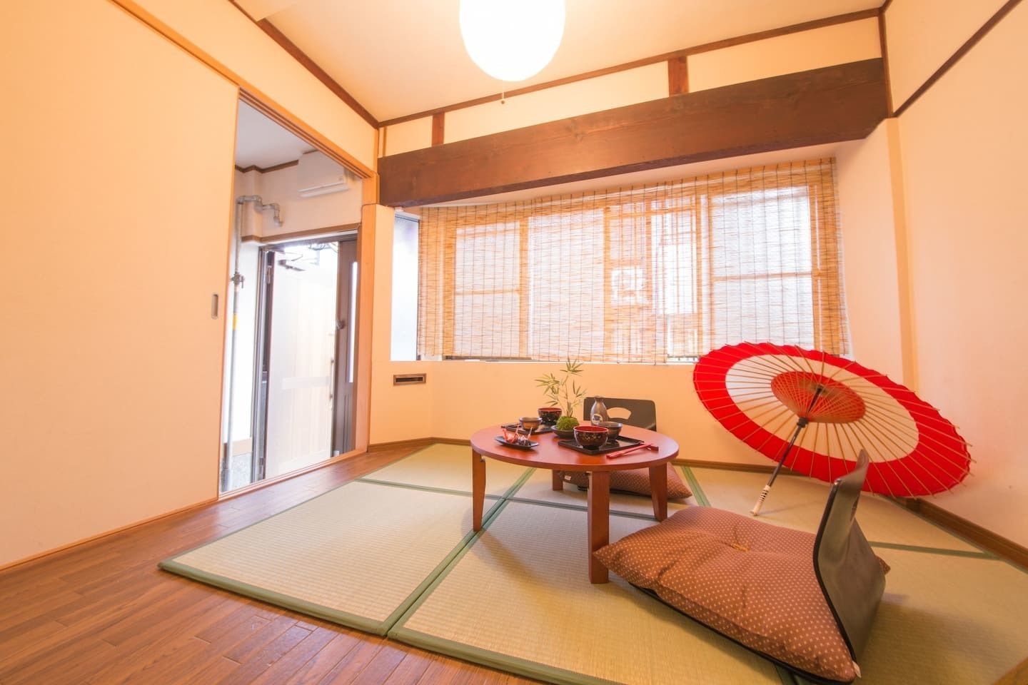 Ett traditionellt japanskt rum med tatamimattor på golvet, en shojiskärm, en röd och vit fläkt och ett bord med teutensilier.