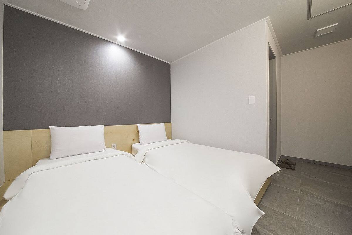 A hotel room with two beds, a grey accent wall, and a tiled floor.