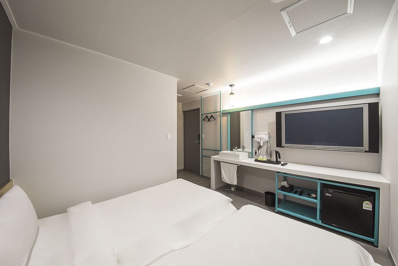 A hotel room with a bed, a TV, a mirror, a sink, and a small fridge.