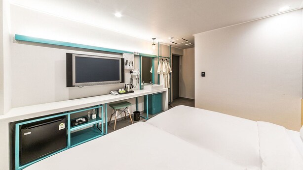 A modern hotel room with a bed, a TV, a desk with a computer, and a bathroom with a mirror and towel rack. - Hannam 67 (Seoul)