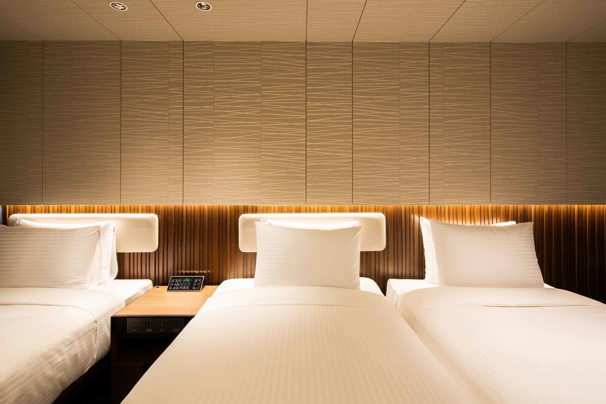 Une chambre d’hôtel avec deux lits, un panneau de commande et un mur recouvert de panneaux de bois.