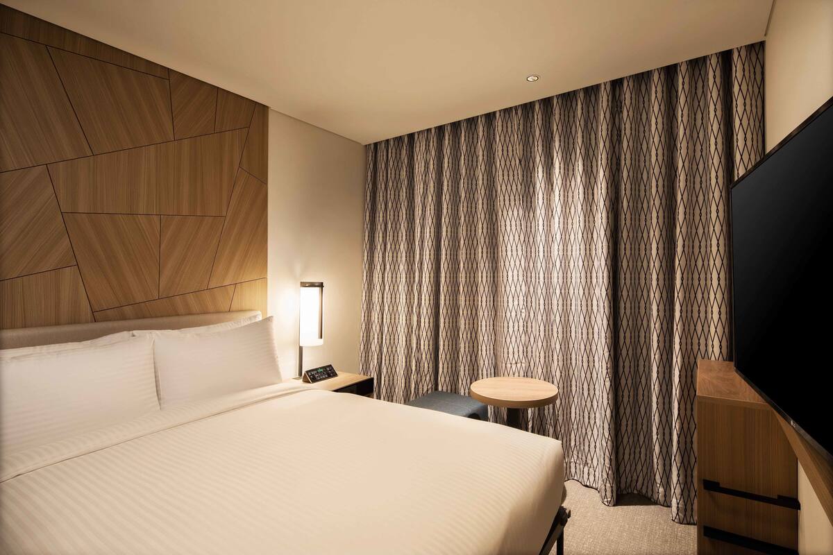 Une chambre d’hôtel avec un grand lit, une petite table, une télévision et des rideaux.