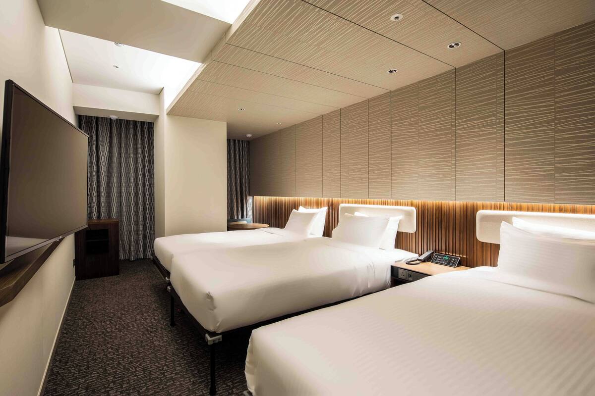 Une chambre d’hôtel avec deux lits, un téléviseur à écran plat, un bureau avec un téléphone et une grande fenêtre.