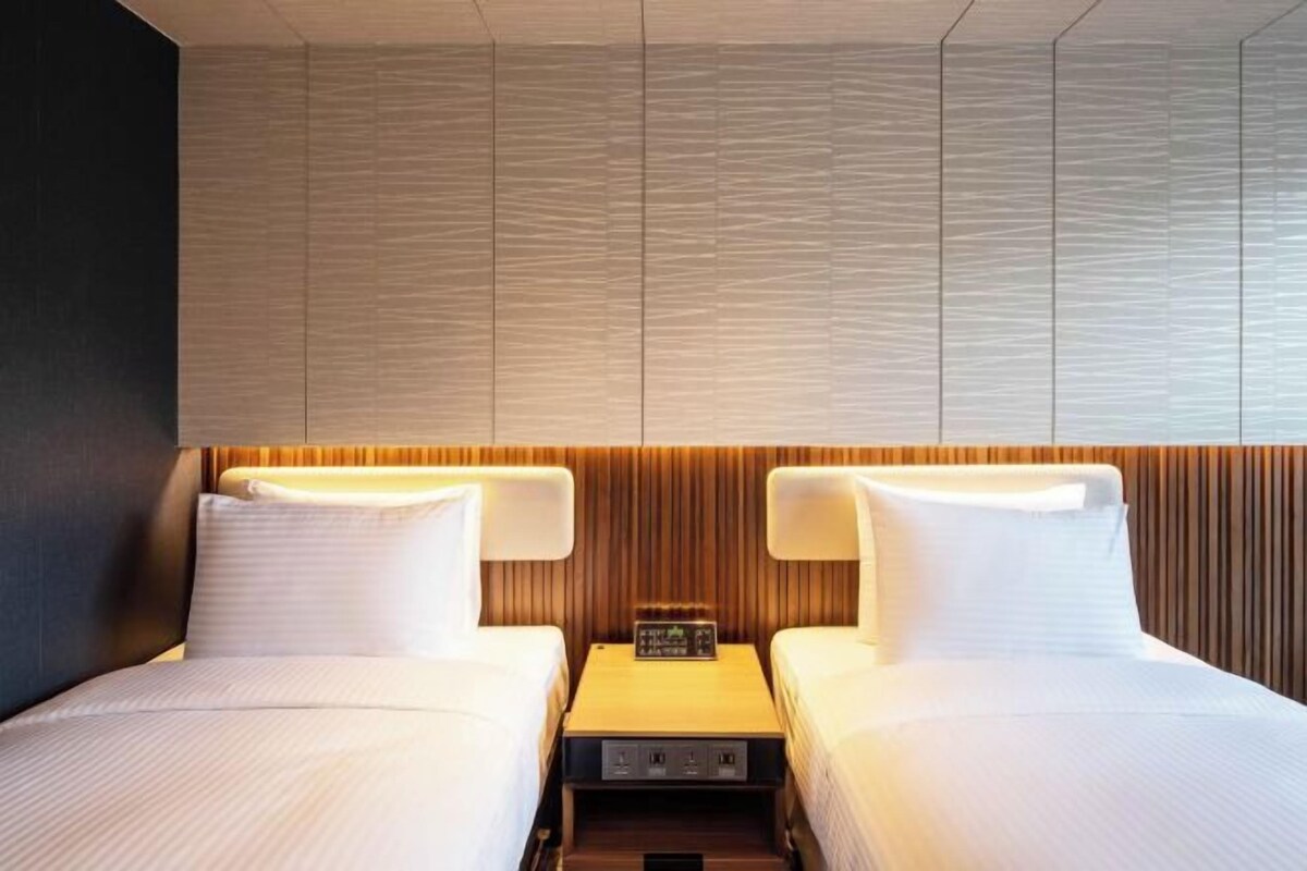 Une chambre d’hôtel avec deux lits, une tête de lit en bois et une table de chevet avec une horloge.