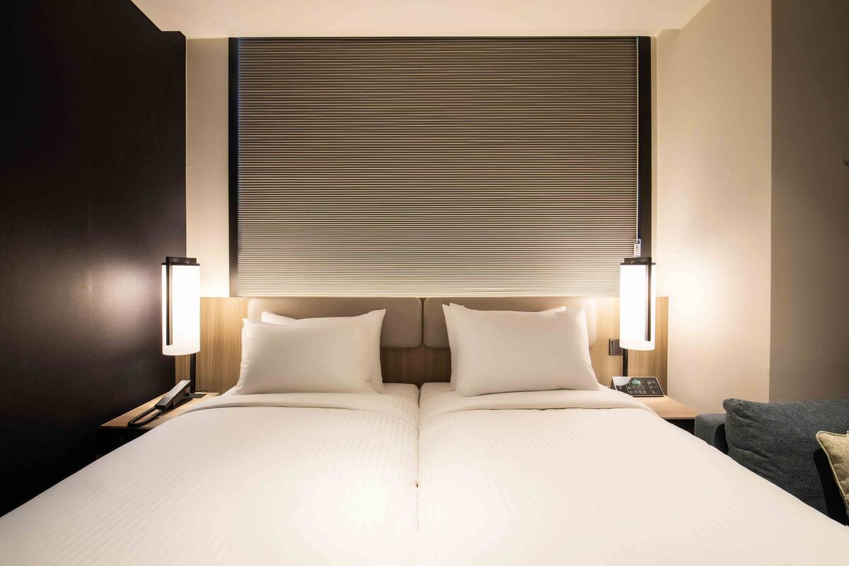 Une chambre d’hôtel avec un grand lit, deux lampes de chevet, une table de chevet et une tête de lit dotée d’un panneau lumineux horizontal.