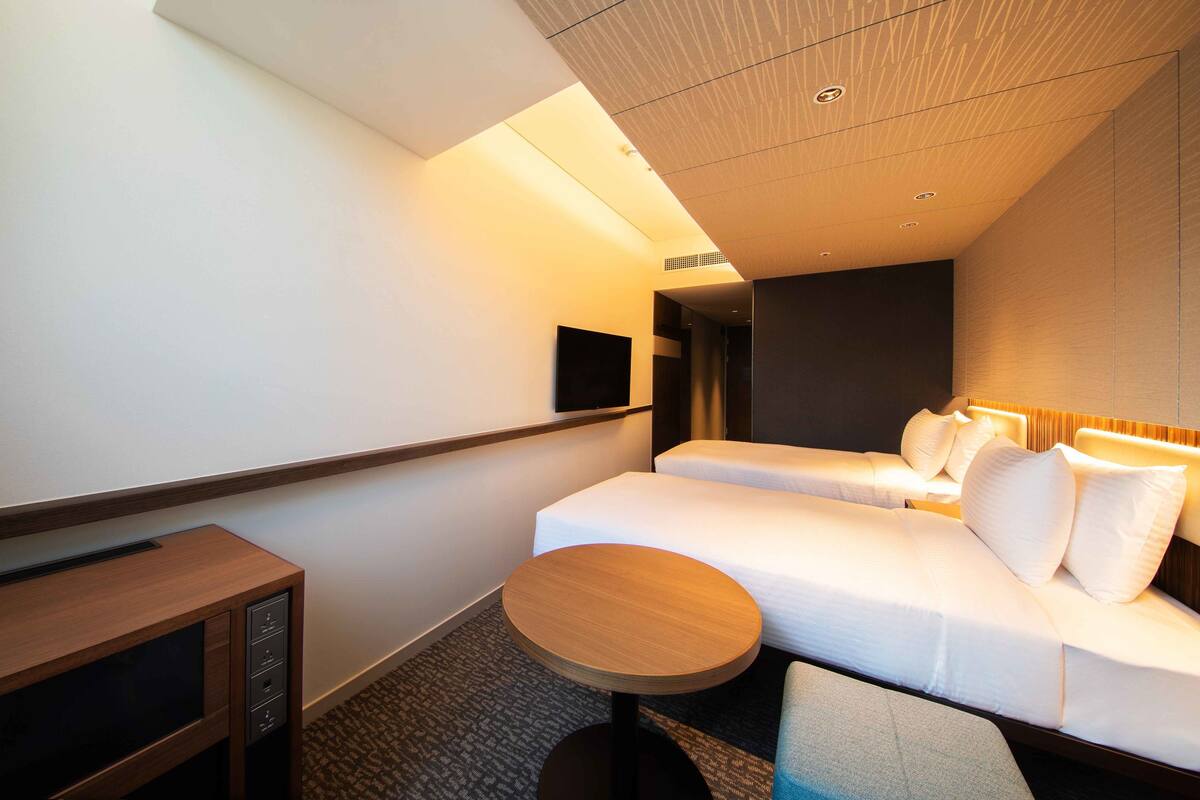 Une chambre d’hôtel avec deux lits, une petite table, un téléviseur et un luminaire au plafond.