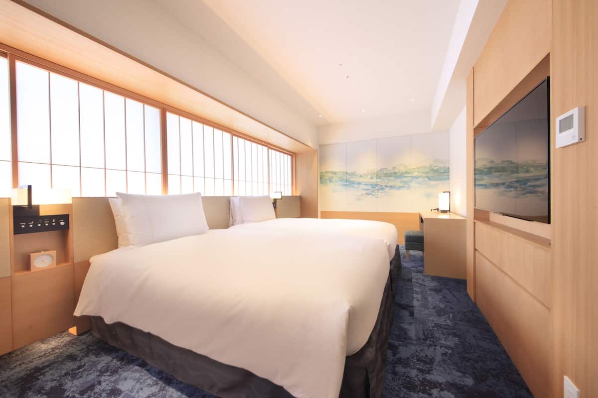 A hotel room with a large bed, a TV, a painting on the wall, and a window with blinds.