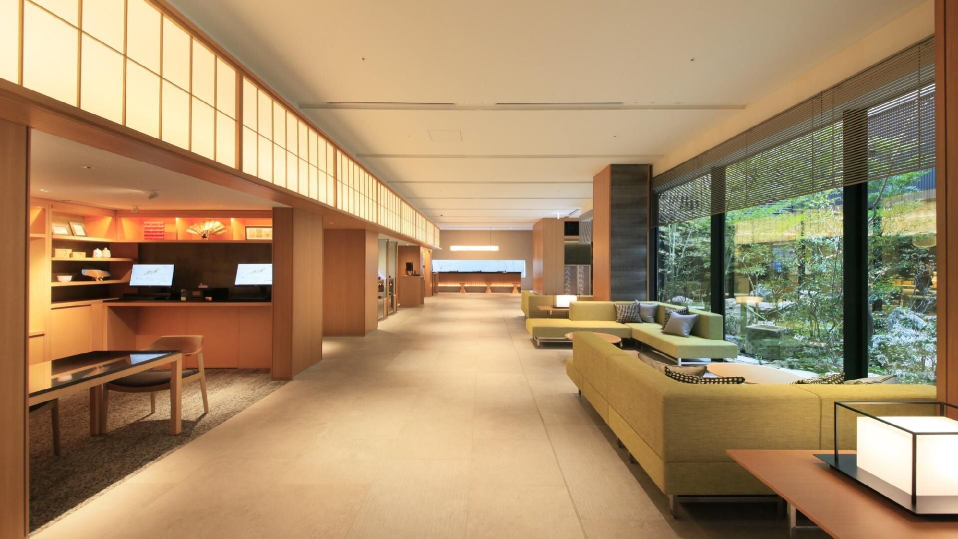 A modern hotel lobby with a reception desk, seating area, and large windows offering a view of the outdoors.