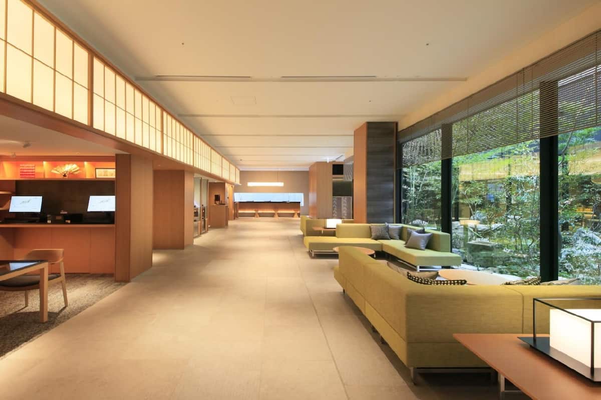 A modern hotel lobby with a reception desk, seating area, and large windows offering a view of the outdoors.
