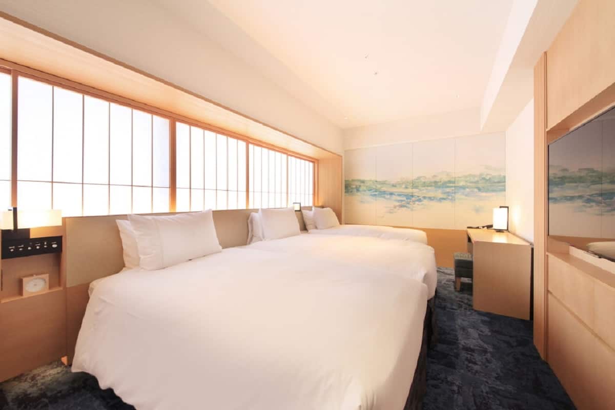 A hotel room with a large bed, a desk, and a window with blinds.