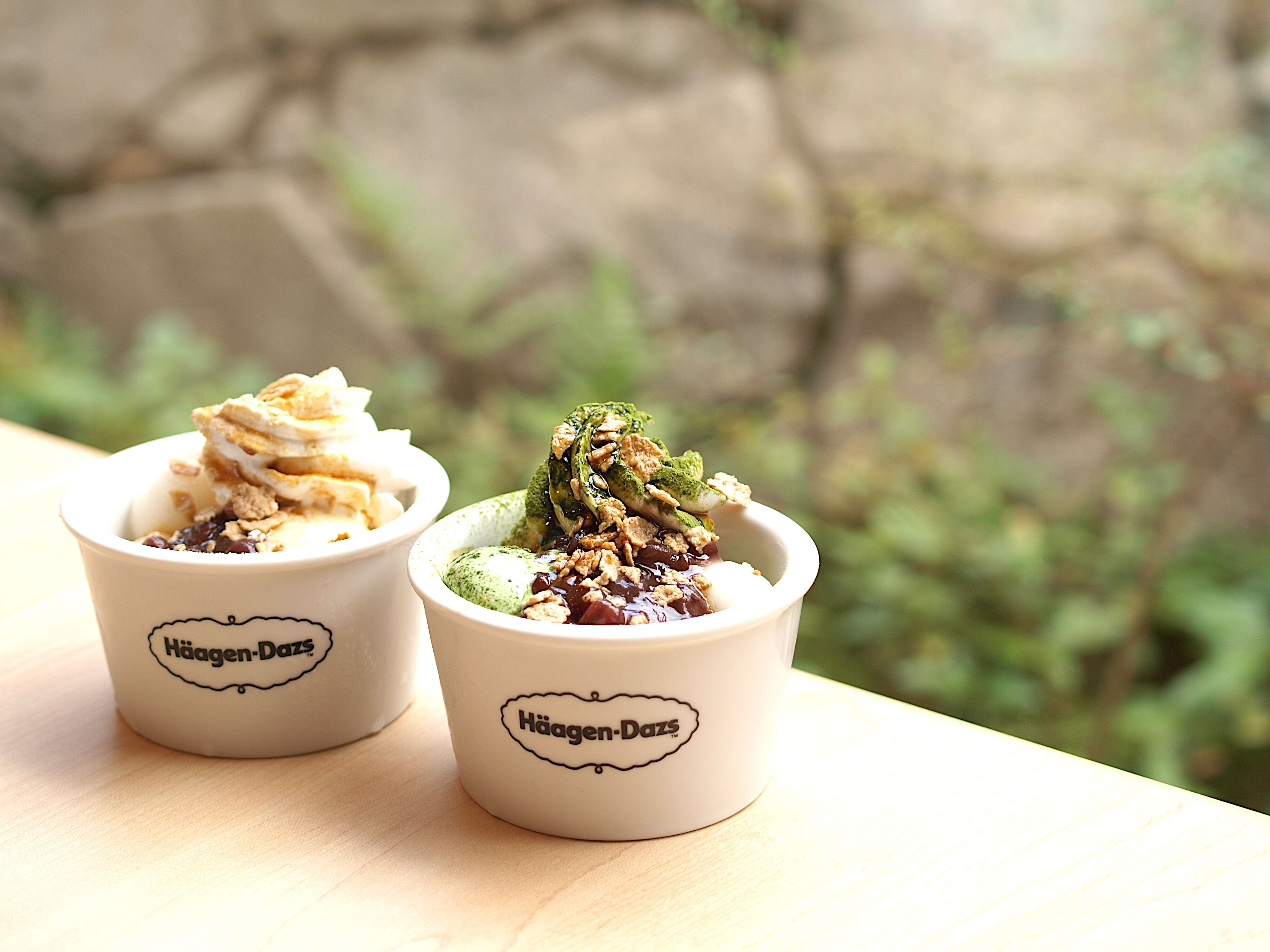 Two Häagen-Dazs dessert cups on a wooden surface with a blurred natural background.