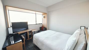 A hotel room with a bed, a desk, a television, and a window.