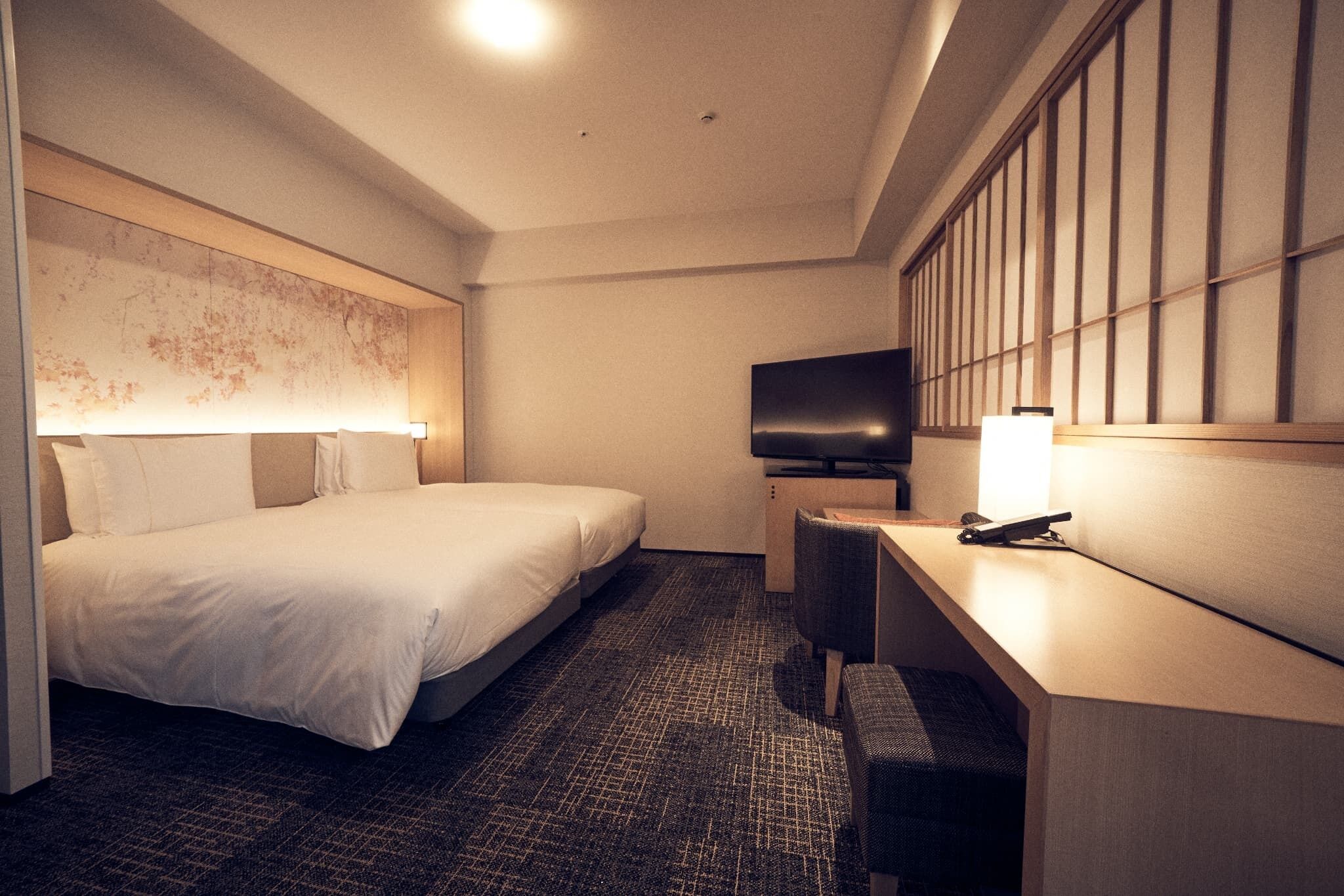 A hotel room with a bed, a desk, a chair, a television, and a wall with a patterned design.