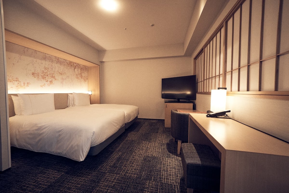 A hotel room with a bed, a desk, a chair, a television, and a wall with a patterned design.