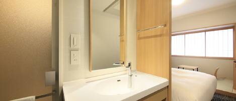 A hotel bathroom with a white sink, a large mirror, and a wooden vanity.