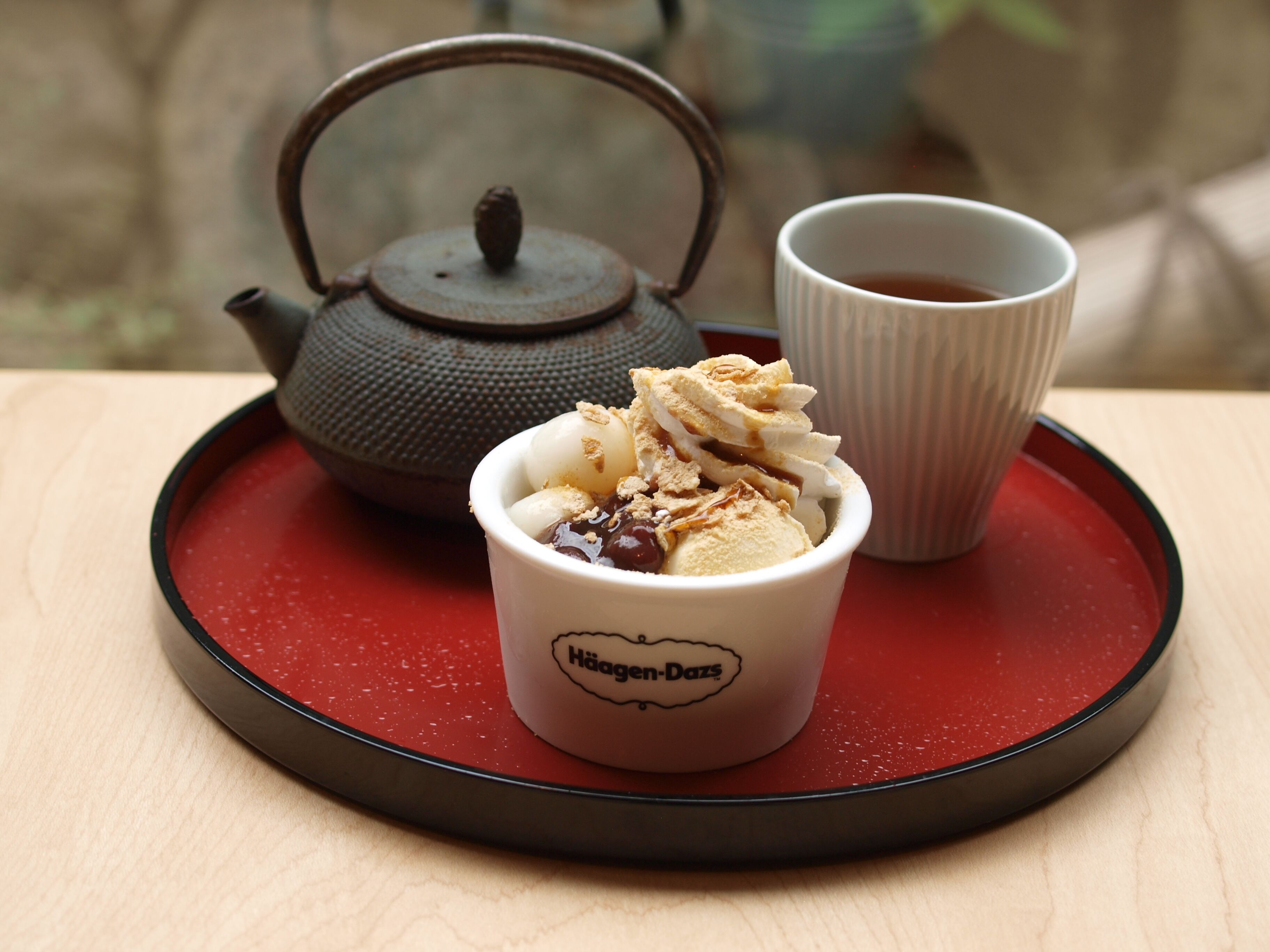 Un postre en una taza con el rótulo "Häagen-Dazs", junto con una tetera y una taza de té sobre una bandeja.