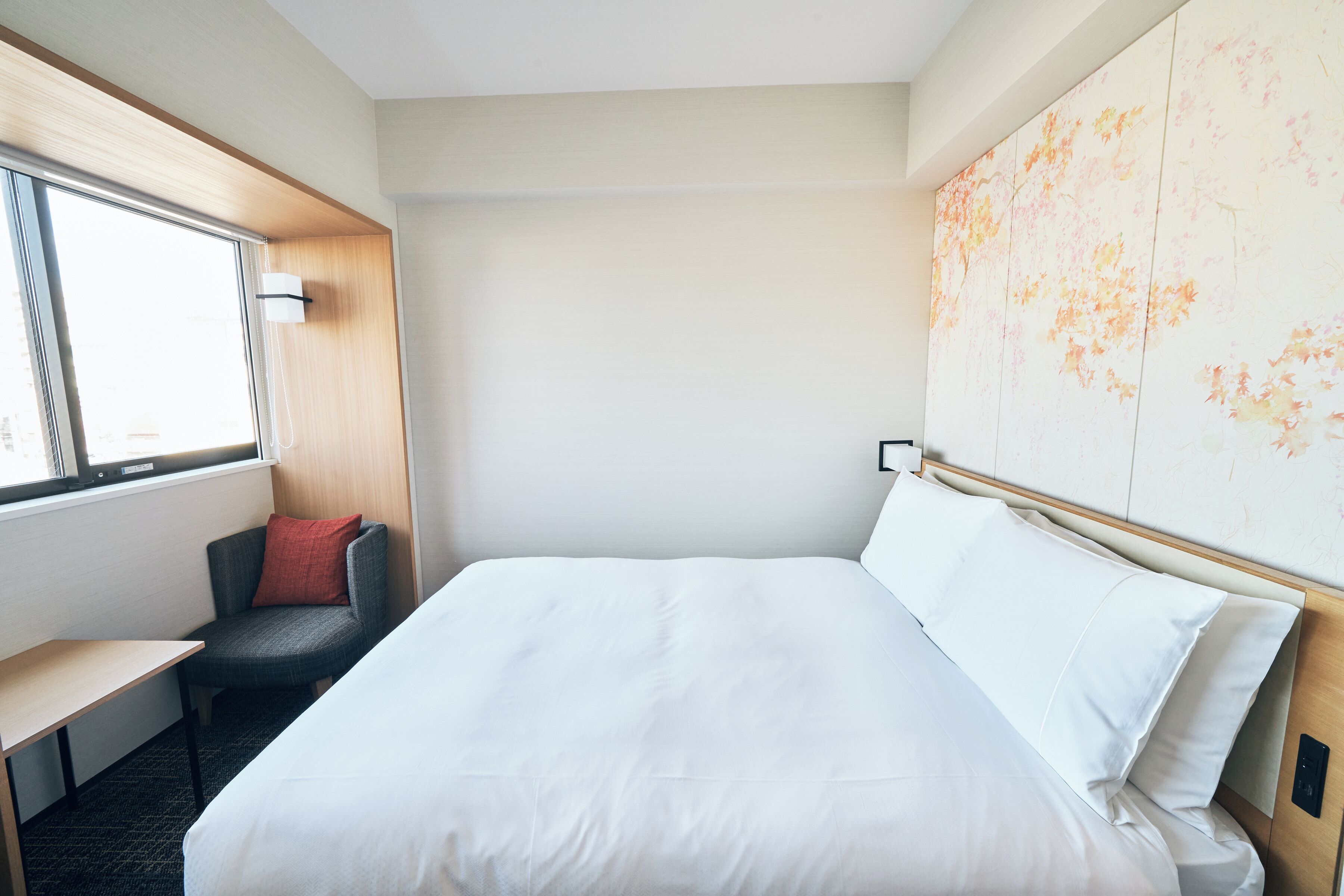 A hotel room with a large bed, a desk, a chair, and a window.