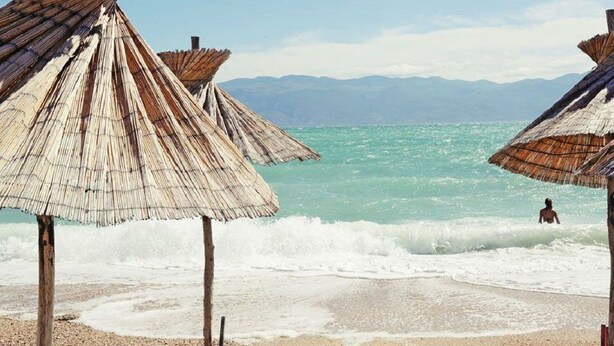 Ein Strand mit Reetdachschirmen und einer Person im Wasser.