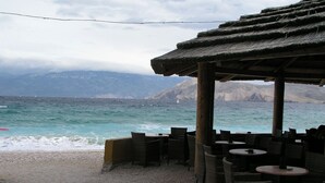 Ein Café direkt am Strand mit Außenbereich, mit Blick auf das Meer und die in der Ferne liegenden Berge.