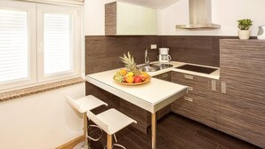 Eine moderne Küche mit weißer Arbeitsplatte, dunklen Holzschränken, einem Edelstahlspülbecken und einer Obstschale auf der Arbeitsfläche.