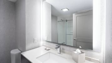 A modern bathroom with a white sink, a glass shower enclosure, and a large mirror.