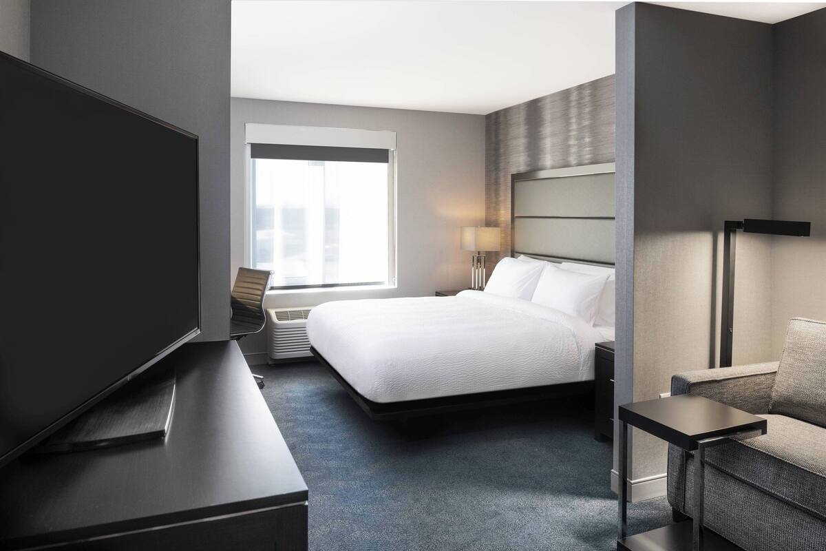 A modern hotel room with a large bed, a flat-screen TV, a desk, and a sofa.