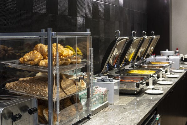 Un bufé con diversos alimentos, entre ellos pasteles y platos calientes, presentados en recipientes transparentes.