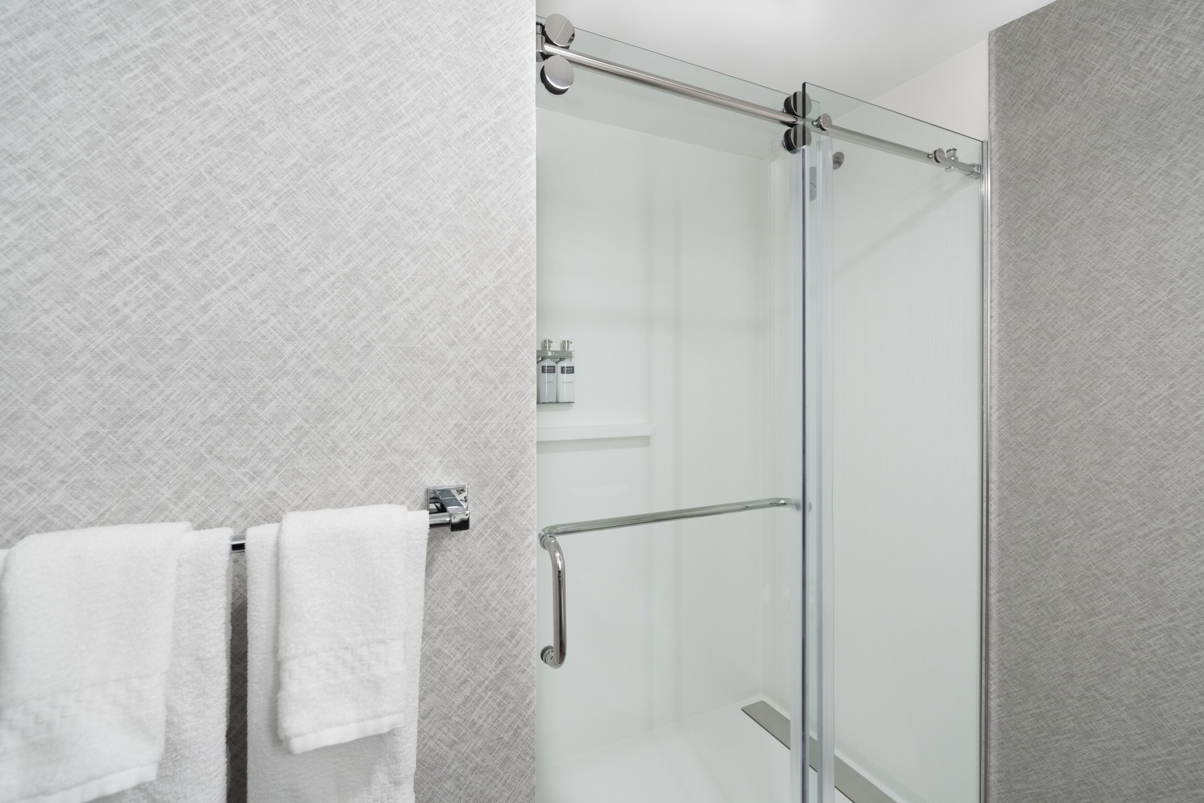Ein modernes Badezimmer mit einer Duschkabine aus Glas, einem Handtuchhalter mit zwei weißen Handtüchern und einer strukturierten Wand.