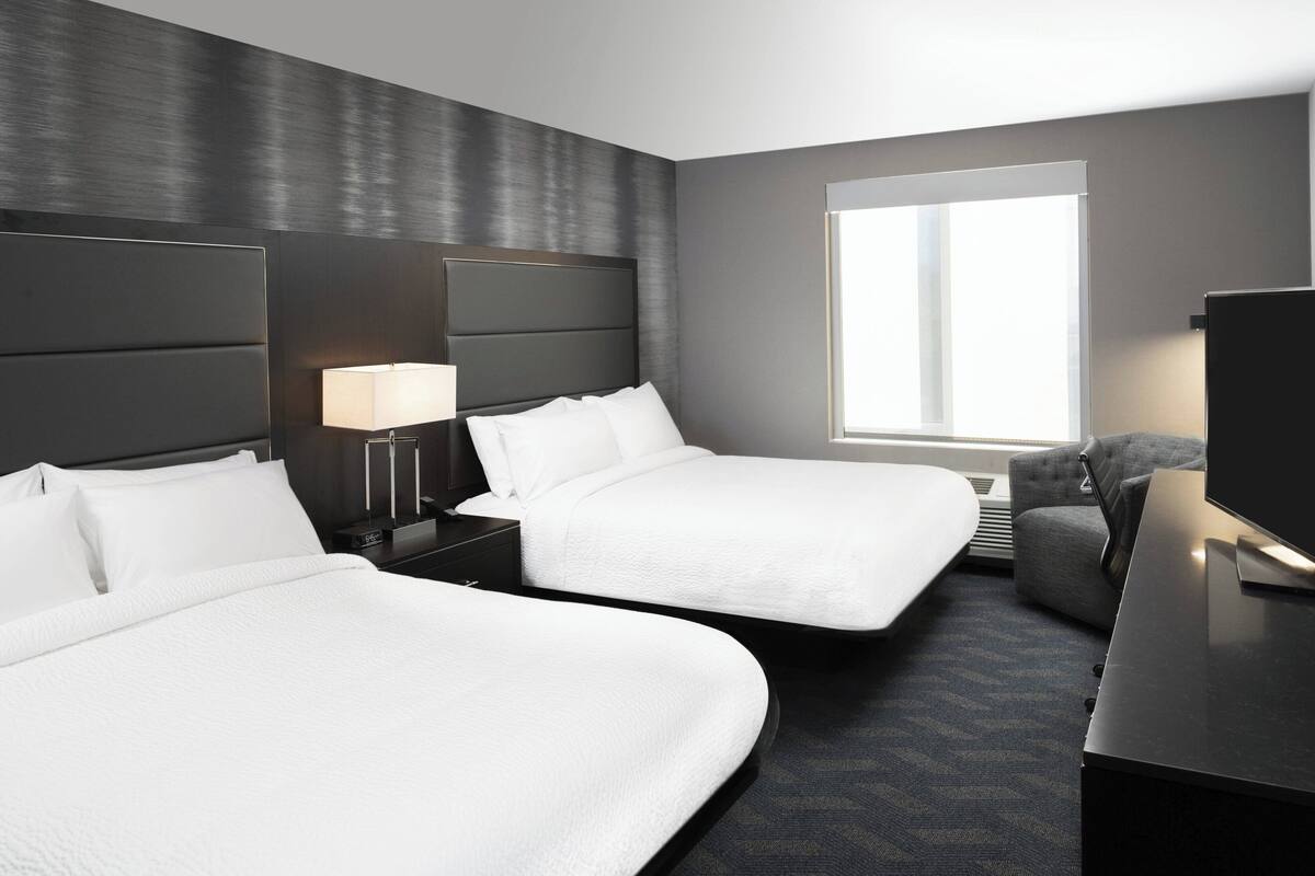 A modern hotel room with two beds, a desk, a TV, and a large window.