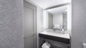 A modern bathroom with a white sink, dark countertop, and a mirror above it. There is a towel rack with folded towels below the sink.