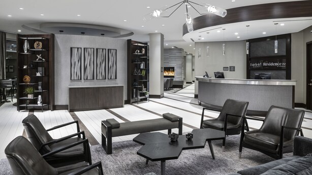 Een moderne hotellobby met een receptiebalie, een zithoek en een open haard.