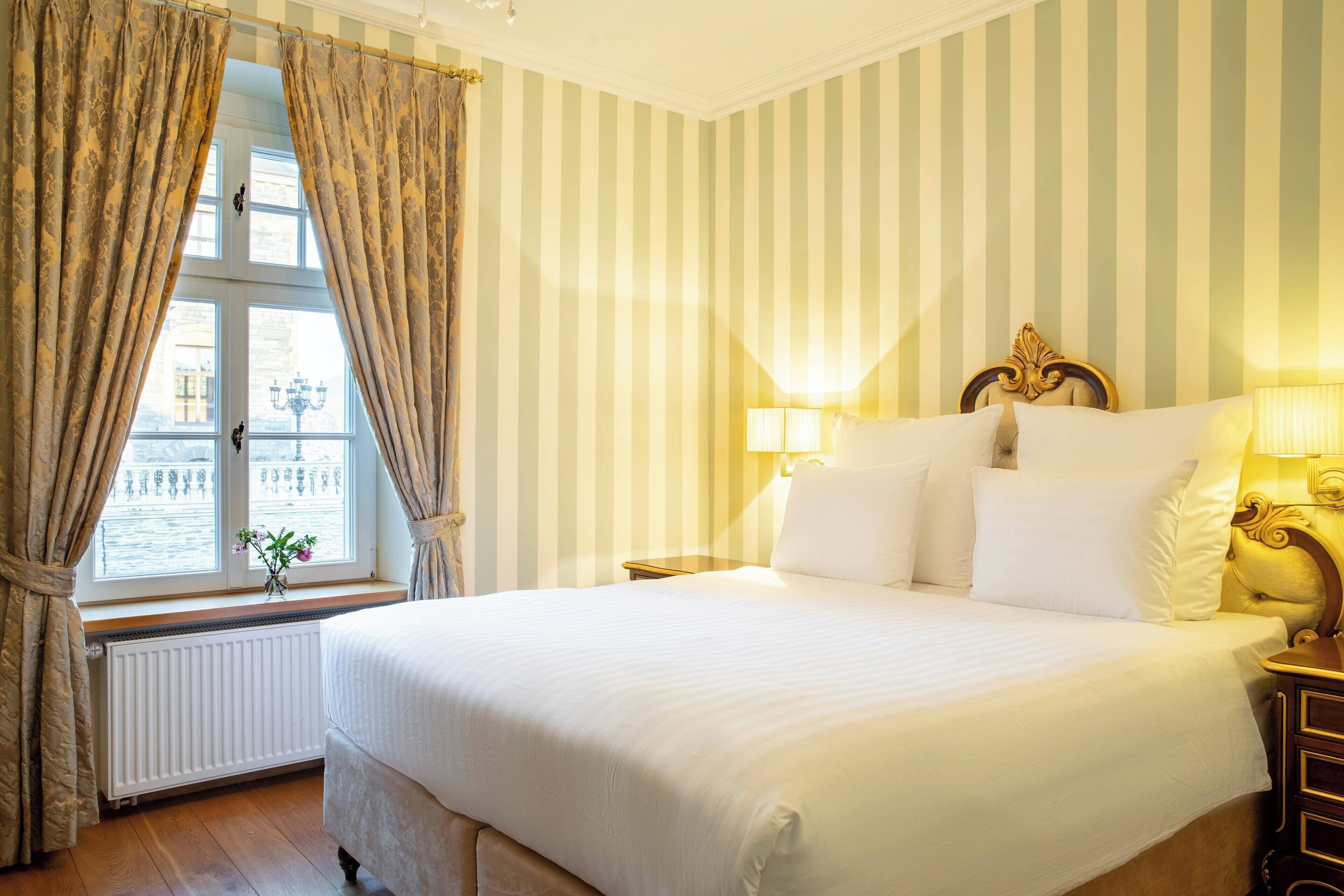 A hotel room with a large bed, striped wallpaper, and a window with curtains.