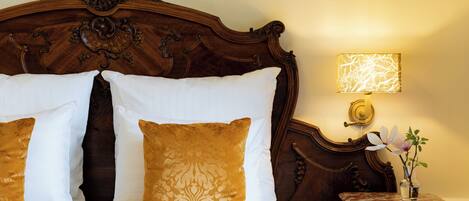 A bed with white and gold pillows, a wooden headboard, and a bedside table with a lamp and a vase of flowers.