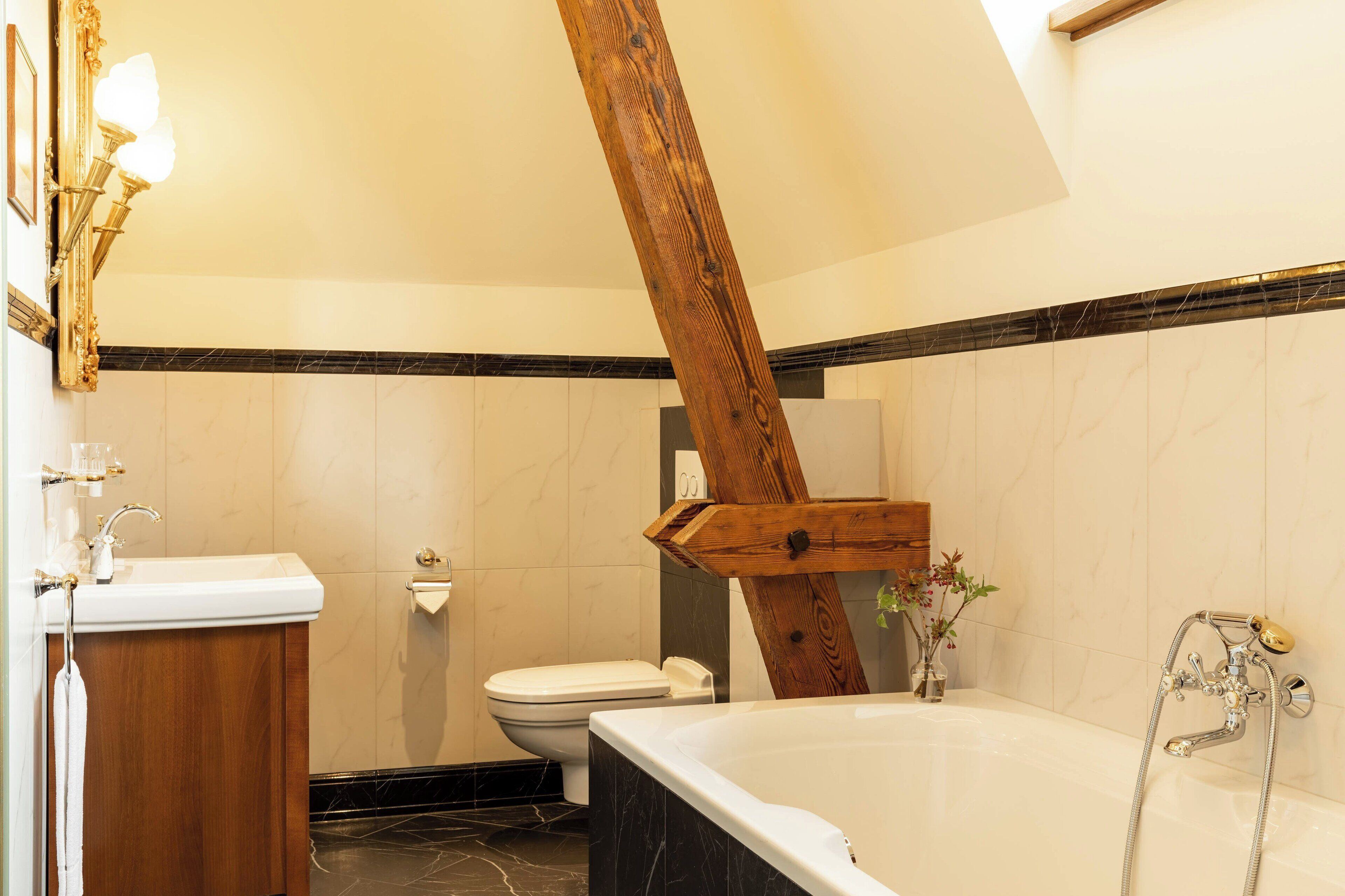 Une salle de bain avec une poutre en bois, une baignoire, un lavabo et des toilettes.