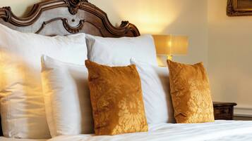Een net opgemaakt bed met witte en gouden kussens, een houten hoofdbord en een bedlampje.