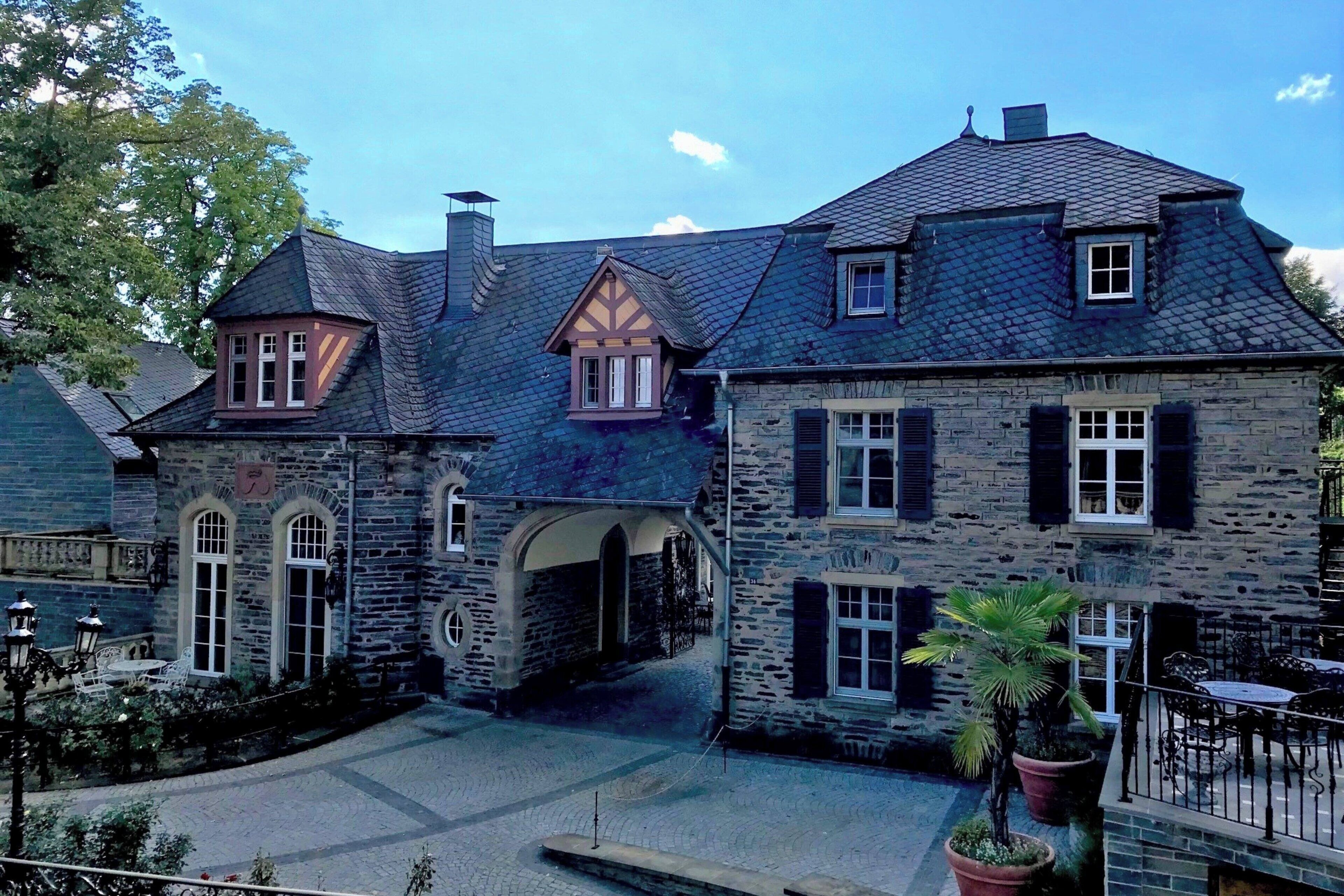 A stone building with a courtyard, featuring a central archway, stone walls, and a small garden area with potted plants.