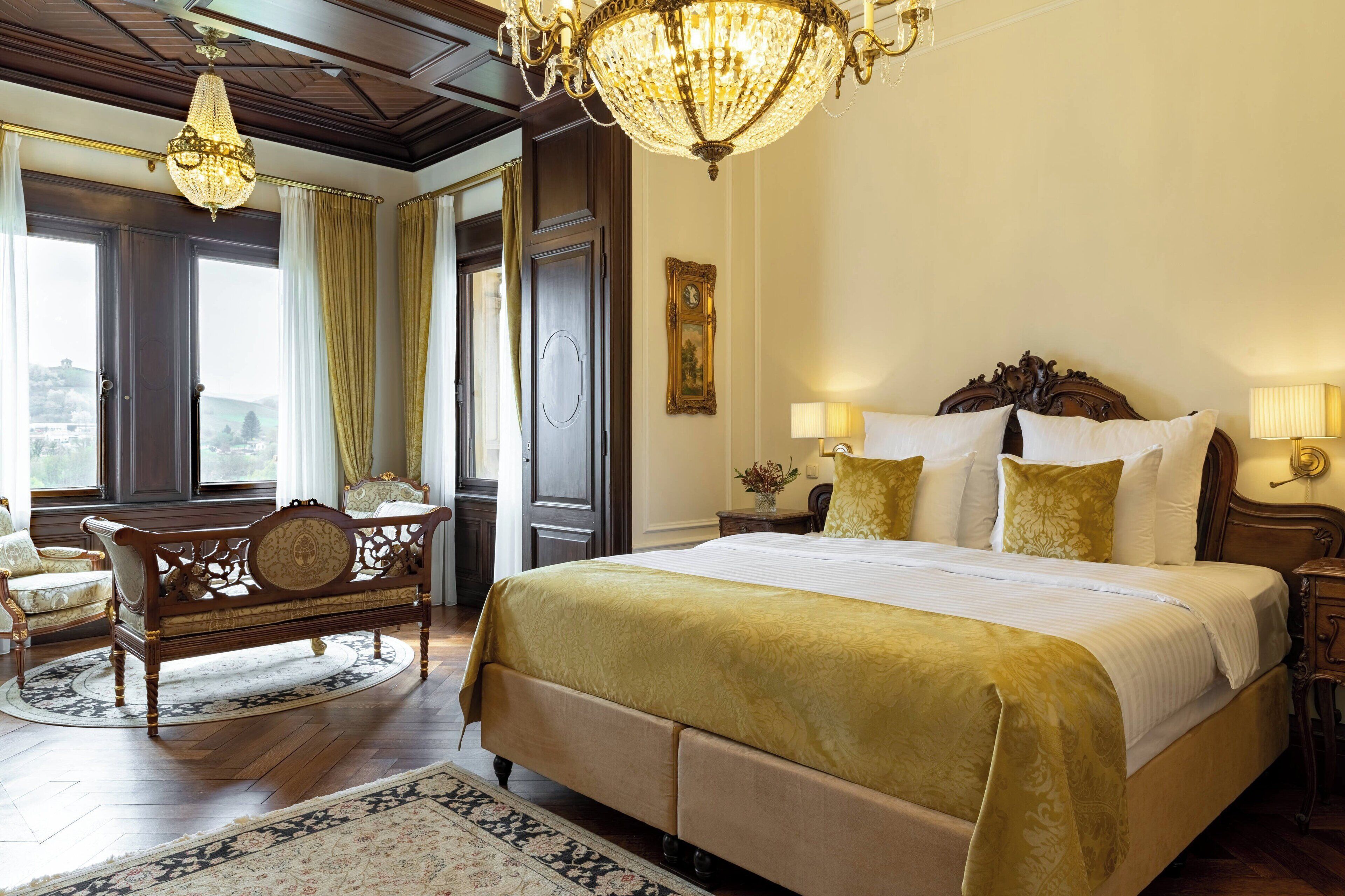 A spacious bedroom with a large bed, ornate wooden headboard, and a chandelier.