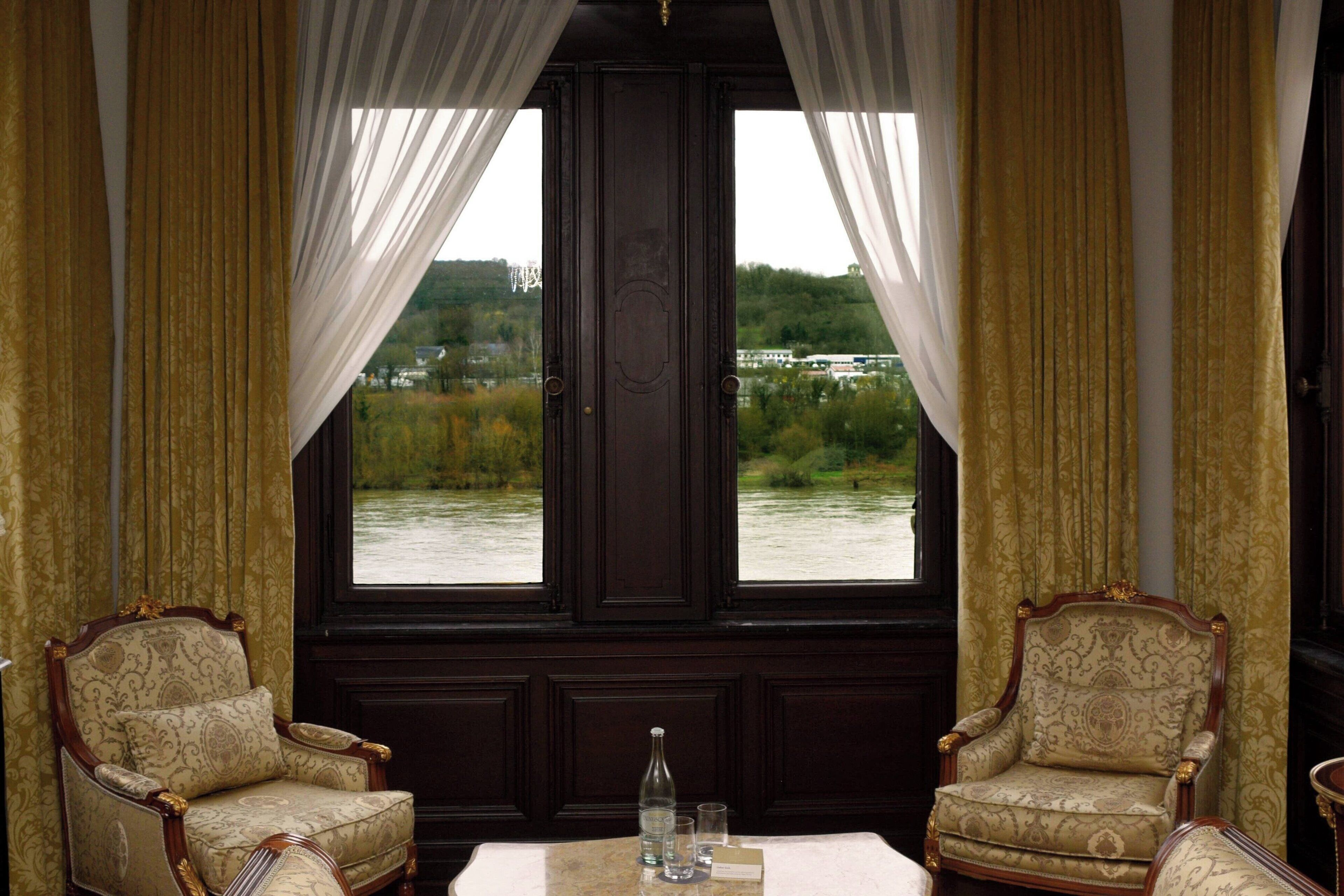 Una habitación con dos sillones decorados, una mesa y vistas a un río.