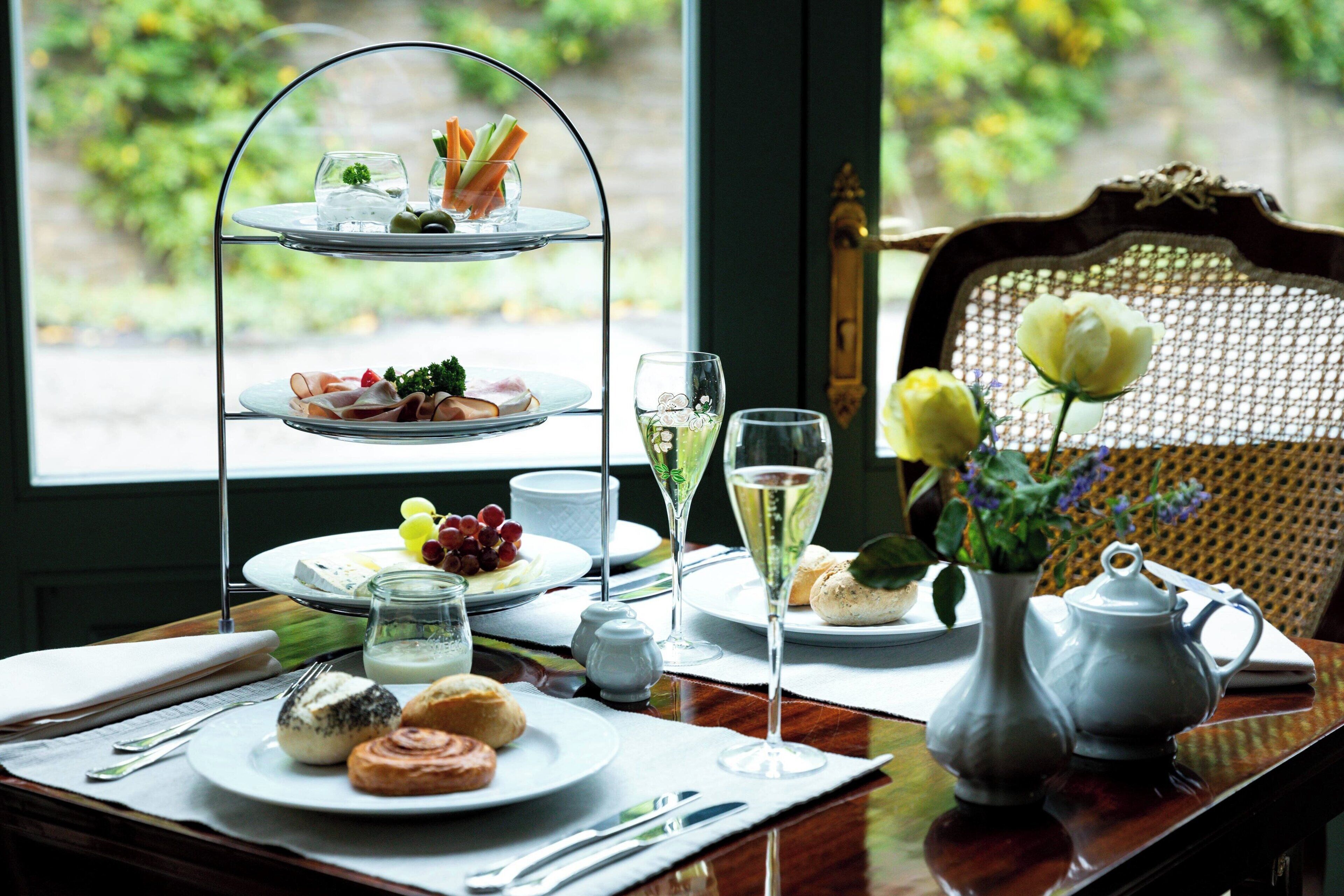 A three-tiered tea service set on a table with plates of pastries, a vase with flowers, and a teapot.